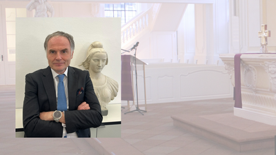 Ein Mann im Anzug, der in die Kamera schaut. Im Hintergrund der Innenraum einer Kirche.