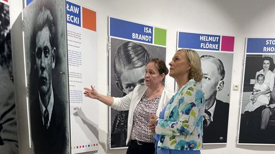 Zwei Frauen vor Tafeln mit Porträtfotos und Texten