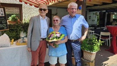 Eine Frau mit Blumenstrauß steht lachend zwischen zwei Männern.