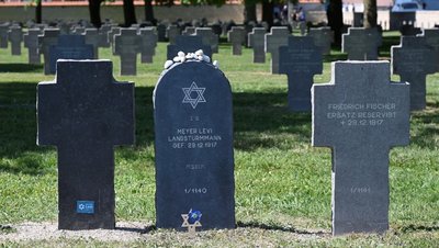 Eine Grabstele zwischen Grabkreuzen auf einem Friedhof